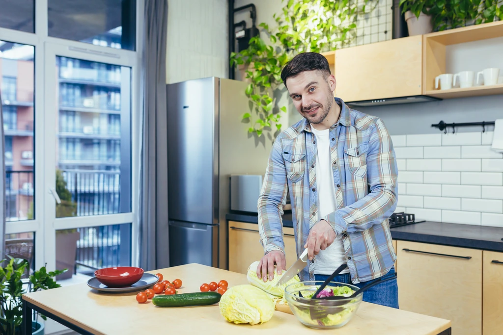 Michael Carter, founder of Delish Symphony, smiling at the camera while chopping fresh cabbage in his home kitchen.