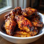 A close-up of a white bowl filled with golden-brown, crispy air fryer chicken wings.