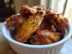 A close-up shot of a white bowl filled with delicious, crispy Air Fryer Chicken Wings, seasoned with herbs.