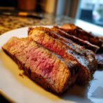 Close-up of perfectly cooked Alton Brown London broil, sliced and served on a white plate, showing a tender pink interior.