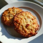 Two golden brown apple pie cookies with visible chunks of apple and spices, resting on a white plate.