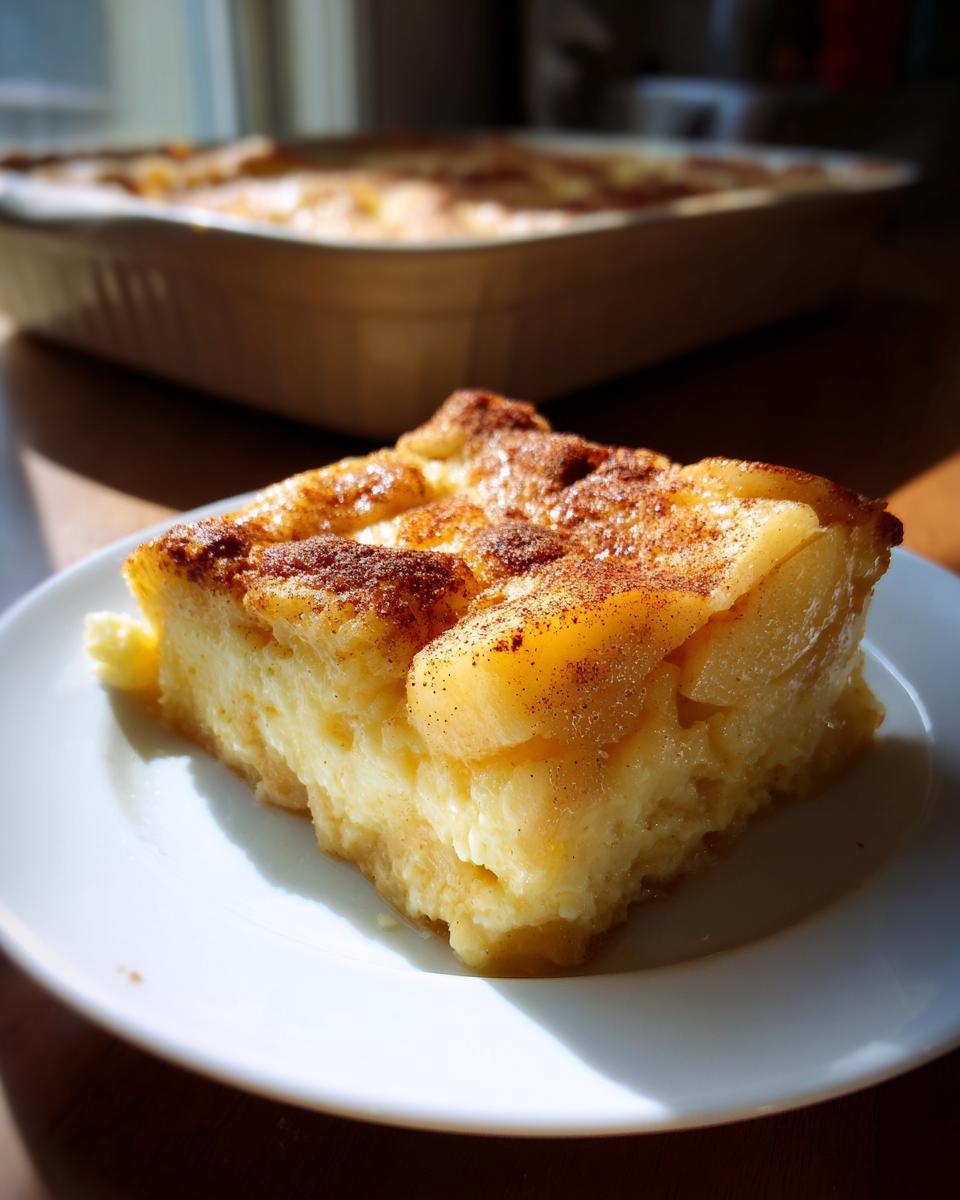 A close-up shot of a slice of apple pie dump cake on a white plate, dusted with cinnamon.