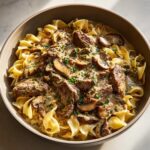 A close-up of a bowl of beef stroganoff with tender beef, mushrooms, and creamy sauce served over egg noodles.