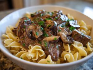 A close-up of a bowl filled with creamy beef stroganoff, tender beef pieces, mushrooms, and egg noodles, garnished with parsley.