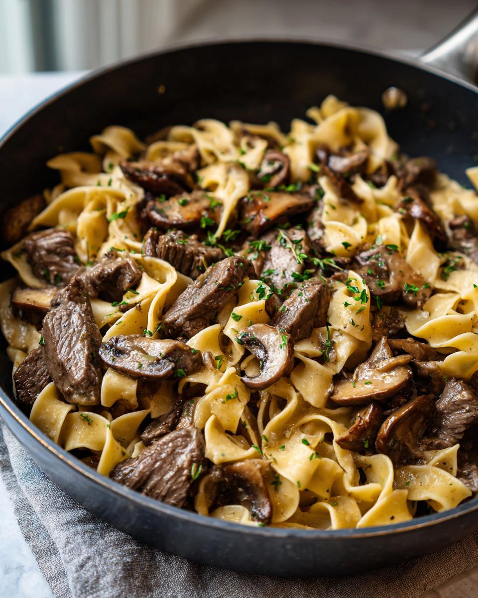 A close-up of delicious Beef Stroganoff with tender beef strips, mushrooms, and egg noodles in a creamy sauce, garnished with parsley.
