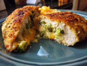 A close-up of a golden-brown breaded chicken breast, sliced to reveal a cheesy broccoli filling, served with Cajun salmon and shrimp.