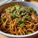 A close-up of savory chipotle chicken noodles, garnished with fresh green onions and sesame seeds.