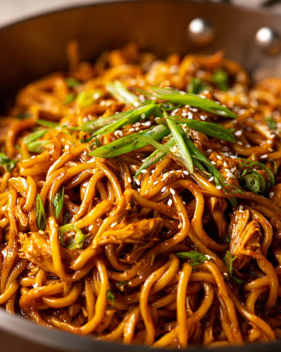 Close-up of savory chipotle chicken noodles garnished with green onions and sesame seeds.