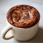 A delicious chocolate protein mug cake topped with peanut butter swirls, ready to be enjoyed.