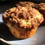Close-up of a golden brown coffee cake muffin topped with a generous cinnamon streusel topping.