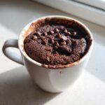 A close-up of a moist Cottage Cheese Microwave Brownie topped with chocolate chips in a white mug.