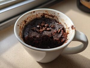 A rich chocolate brownie made with cottage cheese, topped with chocolate chips, served in a white mug.