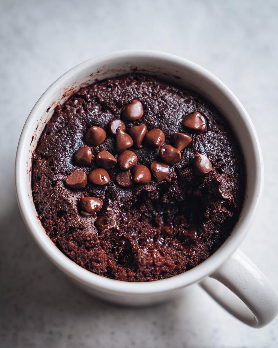 A close-up of a decadent Cottage Cheese Microwave Brownie topped with chocolate chips, with a bite taken out.