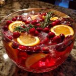 A crystal bowl filled with vibrant Cranberry Orange Punch, featuring ice, fresh cranberries, orange slices, and a sprig of rosemary.