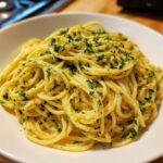 A close-up of a white bowl filled with creamy lemon pasta, generously sprinkled with fresh parsley.