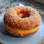 A close-up of a single creme brulee donut, coated in sparkling sugar, with a visible creamy filling.