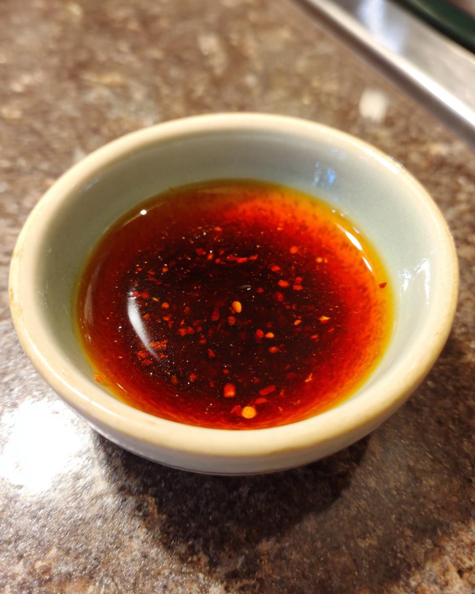 A small bowl filled with a rich, reddish-brown dumpling sauce, speckled with chili flakes.