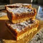 Two delicious pumpkin bars stacked, dusted with powdered sugar, showcasing a rich orange filling and crumbly crust.