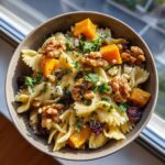 A close-up of a bowl of fall pasta salad featuring farfalle pasta, butternut squash, walnuts, cranberries, and feta cheese.