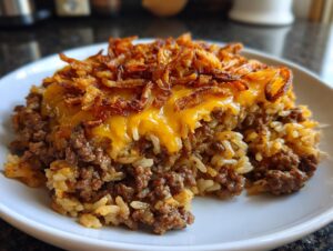 A close-up of a serving of French onion beef over rice, topped with melted cheddar cheese and crispy fried onions.
