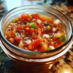 Close-up of fresh tomato canned salsa in a glass jar, showing diced tomatoes, onions, peppers, and cilantro.