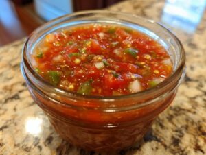 Close-up of a glass jar filled with vibrant fresh tomato canned salsa, showing chunks of tomatoes, jalapeños, and onions.