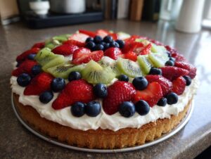 A vibrant fruit pizza sugar cookie topped with whipped cream, strawberries, blueberries, and kiwi.