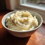 A bowl of fluffy garlic parmesan mashed potatoes topped with herbs.