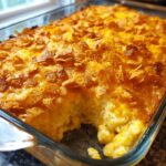 A close-up shot of a freshly baked hashbrown casserole in a glass dish, topped with melted cheese and crushed cereal.