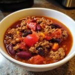 A close-up of a bowl of hearty 1-pot chili, featuring ground beef, kidney beans, black beans, and diced tomatoes.