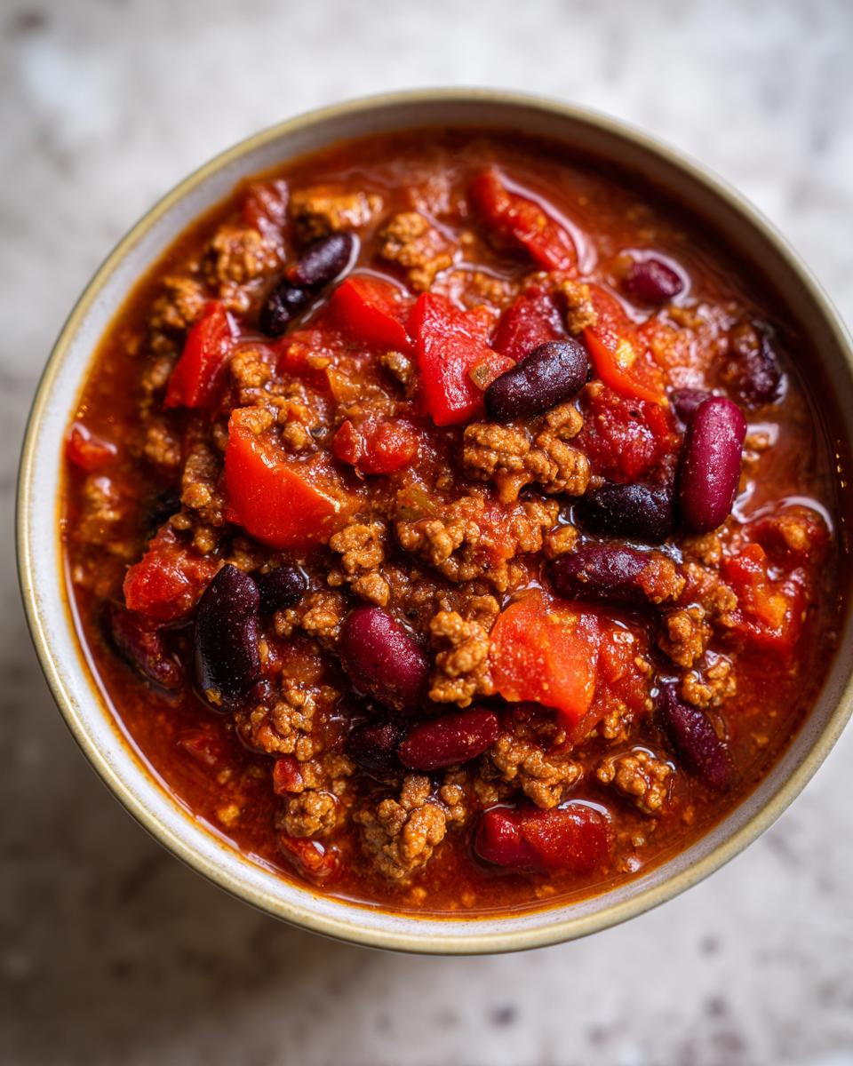 A close-up overhead view of a bowl filled with hearty 1-pot chili, featuring ground meat, kidney beans, and tomatoes.