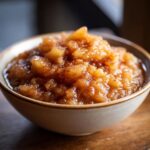 A close-up, appetizing shot of warm, chunky homemade applesauce dusted with cinnamon in a rustic bowl.