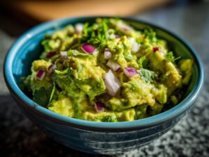 Close-up of vibrant green Homemade Guacamole in a blue bowl, topped with diced red onion and cilantro.