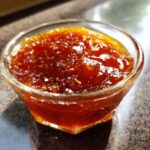 A close-up of rich, glossy honey BBQ sauce in a clear glass bowl, showing its texture and color.