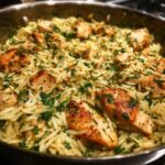 Close-up of a skillet filled with tender lemon chicken orzo, garnished with fresh parsley.
