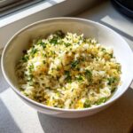A white bowl filled with fluffy Mediterranean lemon rice, garnished with fresh parsley and lemon zest.