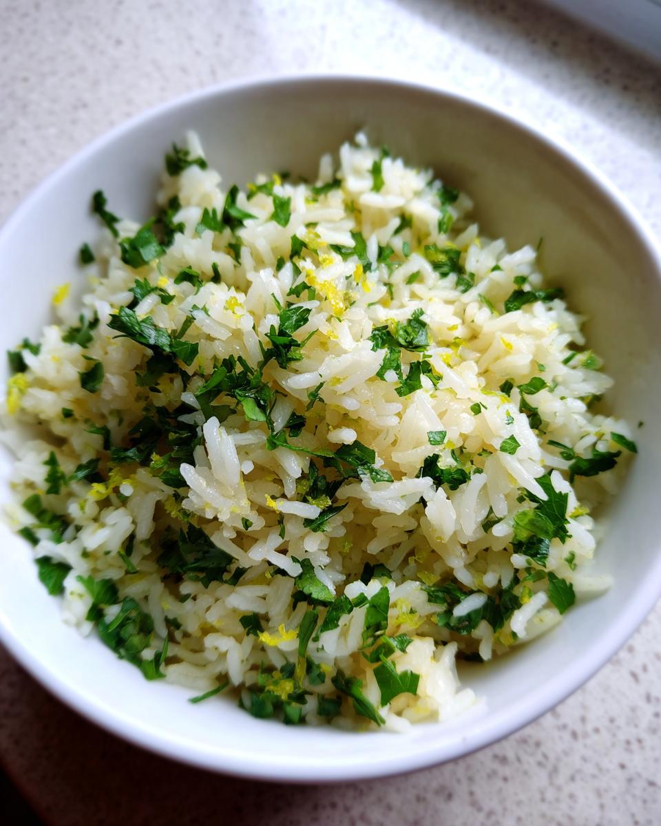A bowl of fluffy Mediterranean lemon rice generously topped with fresh chopped parsley and lemon zest.