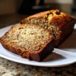 A close-up of a moist banana bread loaf with a slice cut out, showcasing its texture and golden-brown crust.