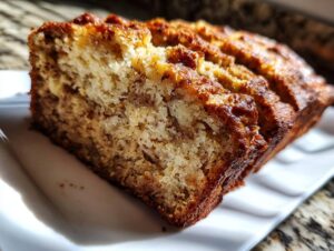 A close-up, angled view of a moist slice of homemade banana bread on a white plate.