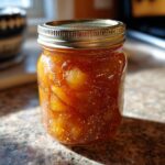 A close-up of a glass jar filled with glistening, old-fashioned pear preserves.