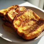 Close-up of golden-brown protein French toast slices sprinkled with cinnamon on a plate.