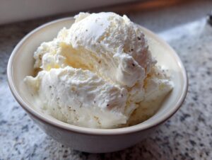 A bowl filled with creamy scoops of homemade protein ice cream, showing its smooth texture and small flecks.