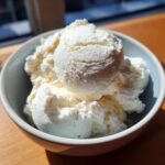 A close-up of creamy, white protein ice cream scooped into a light blue bowl.