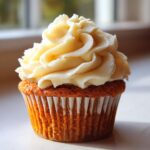 A close-up of a moist pumpkin spice cupcake topped with swirls of creamy frosting.