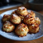 A pile of golden rigatoni bake cookies topped with shredded coconut on a patterned plate.