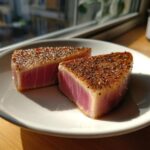 Two perfectly seared tuna steaks, seasoned with pepper, served on a white plate.