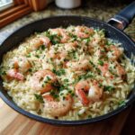 A close-up of shrimp orzo in lemon garlic sauce, garnished with fresh parsley and red pepper flakes.