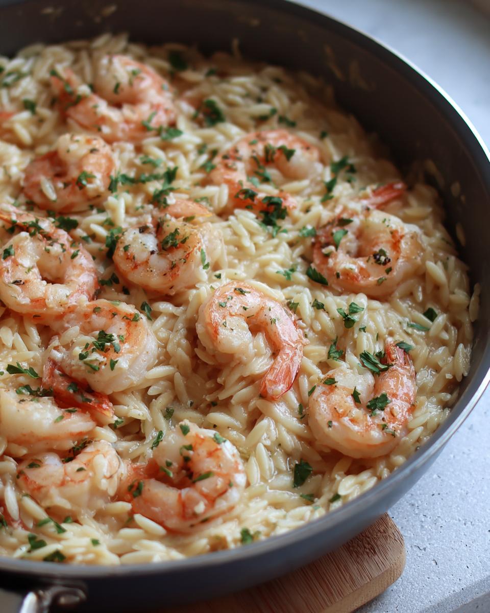 Close-up of shrimp orzo in lemon garlic sauce, garnished with fresh parsley, served in a skillet.