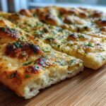 Close-up of soft garlic naan bread topped with melted butter, garlic, and fresh parsley, sliced on a wooden board.