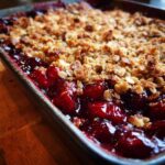 Close-up of a bubbling sour cherry crisp in a baking dish, with a golden oat topping.
